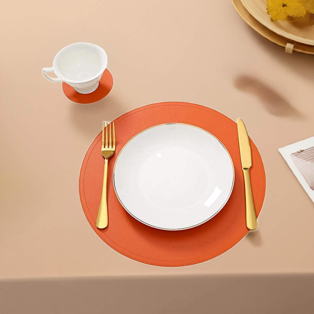 SophistiMat Orange leather placemat and coaster with gold cutlery and white dinnerware on a beige table.